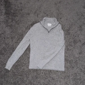 Grå halvzip merinoulltröja från These Glory Days - Säljer en stilren grå tröja i merinoull från These Glory Days. Tröjan har en dragkedja vid halsen och långa ärmar, perfekt för kyligare dagar. Den är mjuk och bekväm, idealisk för både vardag och mer avslappnade tillfällen. Storlek M men passar mer S 