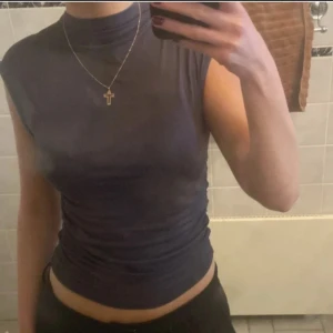 Mörkgrå ärmlös polotopp - Säljer en stilren mörkgrå ärmlös polotopp. Perfekt för lager-på-lager eller att bära som den är. Toppens material är mjukt och stretchigt för en bekväm passform.