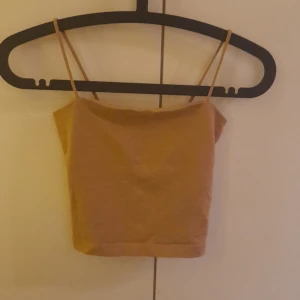 Beige tubtopp från Gina Tricot - Säljer en stilren beige tubtopp från Gina Tricot. Toppen har smala axelband och en enkel design som passar perfekt till sommaren. Perfekt för att matcha med jeans eller kjol för en avslappnad look.
