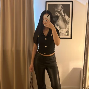 Svart kortärmad topp med knappar - Snygg svart kortärmad topp med dekorativa knappar i guld. Toppen har en v-ringad design och är croppad för en modern look. Perfekt för att ge en stilren touch till din outfit. Den är aldrig använd och i helt nytt skick! 