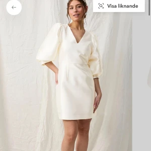 Vit klänning från Joelle - Elegant vit klänning från Joelle med v-ringning och puffiga trekvartsärmar. Perfekt för student och liknande! Slutsåld på deras hemsida och nypris ligger på 999kr. Aldirg använd med lappen på