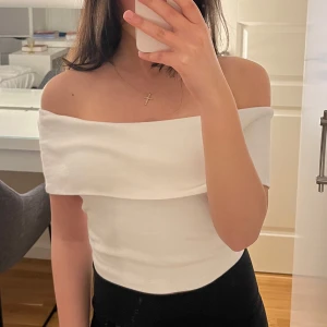 Vit offshoulder topp - Säljer en stilren vit offshoulder topp med en elegant design. Perfekt för en chic och modern look. Toppen har en smickrande passform och är tillverkad i ett mjukt material.