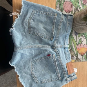 Blå jeansshorts med fransar - Snygga blå jeansshorts med fransiga kanter och klassisk femficksdesign. Perfekta för en avslappnad stil. De har en knappgylf och bälteshällor för extra stilpoäng.