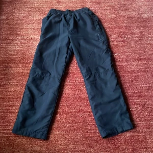 Svarta träningsbyxor från Champion - Säljer ett par svarta träningsbyxor från Champion. Byxorna har en elastisk midja och är tillverkade i ett syntetmaterial som är perfekt för sport och träning. De har en rak passform. I bra skick! 