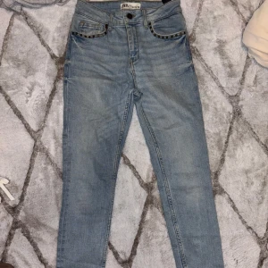 Blå jeansbyxor med nitar - Snygga blå jeansbyxor från Zara med hög midja och raka ben. Byxorna har coola nitar vid fickorna och en klassisk femficksdesign. Perfekta för en trendig look. Sitter riktigt snyggt i bakdelen. 