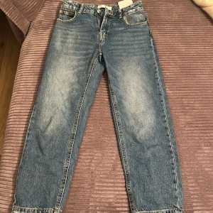 Blå jeans från Zara - Säljer ett par klassiska blå jeans från Zara. De har en rak passform och är tillverkade i denim med en knapp och dragkedja framtill. Perfekta för en avslappnad stil.