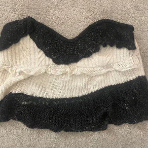 Vit och svart tubtopp från Zara - Säljer en snygg vit och svart tubtopp från Zara. Toppen är stickad med svarta spetsdetaljer upptill och nedtill. Perfekt för en trendig look!