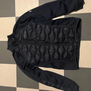 Svart jacka från Peak Performance - Säljer en svart jacka från Peak Performance med quiltad design och dragkedja framtill. Jackan har långa ärmar och en stilren look, perfekt för höst och vår väder. Sitter bra som S-M