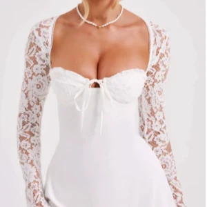 Vit klänning med spetsdetaljer - Elegant vit klänning med långa spetsärmar och en söt knytning framtill. Perfekt för speciella tillfällen. Köpt på Avora fashion men helt oanvänd. Säljer den både i S och M.