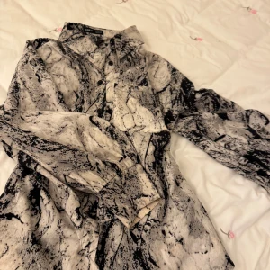 Mönstrad skjorta från Shein - Snygg mönstrad skjorta från Shein i svart och beige. Skjortan har långa ärmar och knappar framtill. Perfekt för en unik stil med sitt abstrakta mönster.