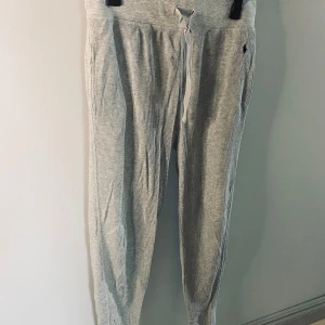 Grå mjukisbyxor från Polo Ralph Lauren - Grå mjukisbyxor från Polo Ralph Lauren med ribbad struktur och snörning i midjan. Byxorna har en broderad logotyp på sidan och ser lite mer ”klädda” ut än vanliga mjukisbyxor.
