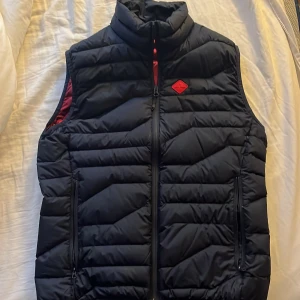 Mörkblå J. Lindberg dunväst med röd insida - Mörkblå J. Lindberg väst med röd insida