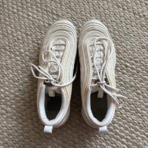 Vita Nike - Säljer ett par vita Nike sneakers med synlig luftdämpning i sulan och klassisk snörning. Skorna har en stilren design med Nike-loggan på sidan.