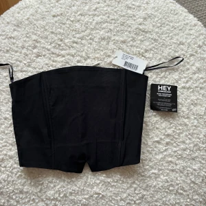 Svart korsettopp från Nelly - Snygg svart korsettopp från Nelly med elastisk rygg för en bekväm passform. Perfekt för att styla med olika outfits. Toppen är i ett stilrent och enkelt utförande.