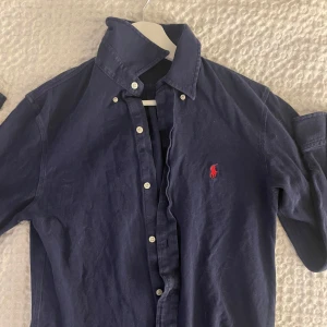 Mörkblå skjorta från Ralph Lauren - Snygg mörkblå skjorta från Ralph Lauren med klassisk krage och knappar. Den har en broderad röd logotyp på bröstet och är tillverkad i ett lätt och bekvämt material. Perfekt för sommaren elelr våren! skriv för fler frågor/bilder 👍