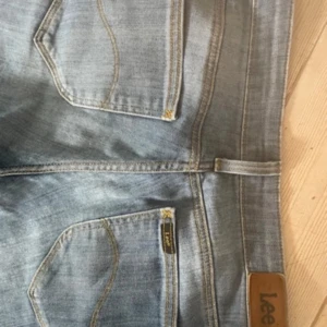 Blå jeans från Lee - Snygga blå jeans från Lee med klassisk femficksdesign och en bekväm passform. De har en rak stil och är perfekta för en avslappnad look. Märkeslogga på baksidan av midjan. De har låg midja/mid. De är klippta själv där nere som syns på bilden W26 och L33- storlek S