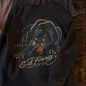 Svart tröja med pantermotiv från Ed Hardy - Säljer en svart tröja från Ed Hardy med ett stort pantermotiv och texten 'Ed Hardy 1971' på framsidan. Tröjan har långa ärmar och en klassisk passform. Perfekt för dig som gillar djärva tryck och unik stil.