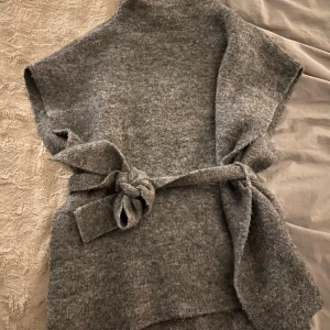 Grå stickad tröja/väst med knytband - Säljer en mysig grå stickad tröja med knytband i midjan. Tröjan har en lös passform och är ärmlös, vilket gör den perfekt för lager-på-lager. Märket Zign❣️