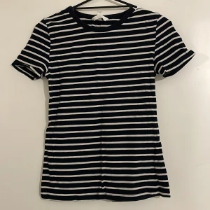 Randig kortärmad topp - Säljer en stilren randig topp i svart och vit med korta ärmar. Perfekt för en avslappnad look. Toppen har en rund halsringning och är gjord i ett mjukt material.