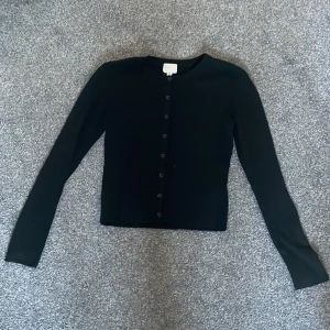 Svart kofta från H&M - Snygg svart kofta från H&M med knappar framtill. Den har långa ärmar och en klassisk rund halsringning. ❤️