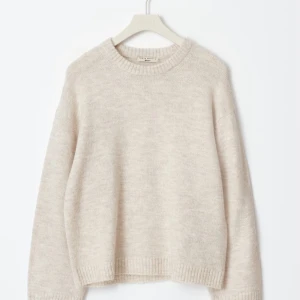 Beige stickad tröja från Gina  - Säljer en stilren beige stickad tröja från Gina. Tröjan har en avslappnad passform med långa ärmar och ribbade kanter vid hals, ärmslut och nederkant. Perfekt för kyligare dagar och enkel att matcha med olika outfits.