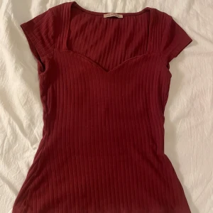 Vinröd ribbad topp - Snygg vinröd ribbad topp från Zara med korta ärmar och en v-ringad hals. Perfekt för en stilren look. Passar bra till både jeans och kjol.