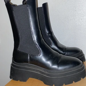 Svarta chelsea boots med platåsula - Snygga svarta chelsea boots i skinn med hög platåsula. De har elastiska paneler på sidorna för enkel på- och avtagning. Perfekta för att ge lite extra höjd och stil till din outfit.