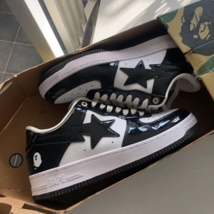 Svartvita sneakers från BAPE - Snygga svartvita sneakers från BAPE med en glansig finish. Skorna har en ikonisk stjärndetalj på sidan och BAPE-loggan på sulan. Perfekta för en stilren look.