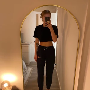 Svarta mjukisbyxor med broderad logga - Säljer ett par svarta mjukisbyxor med broderad logga på benet. Byxorna har en bekväm passform med dragsko i midjan för justering. Perfekta för en avslappnad stil.