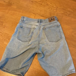 Ljusblå jeansshorts från Sweet SKTBS - Snygga ljusblå jeansshorts från Sweet SKTBS med klassisk femficksdesign och knappgylf. Perfekta för en avslappnad stil med en touch av skandinavisk heritage. Märkesdetaljer på knappen och etiketten ger en extra cool vibe.