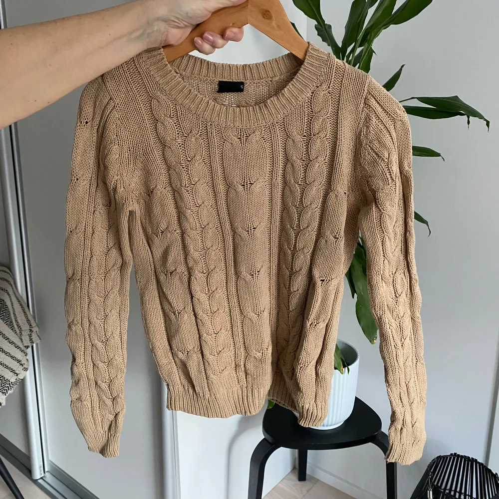 Säljer en snygg beige stickad tröja med flätmönster. Tröjan har långa ärmar och en rund halsringning. Perfekt för kyligare dagar och ger en mysig känsla. Passar bra till både jeans och kjol.. Neuletakit & Villapaidat.