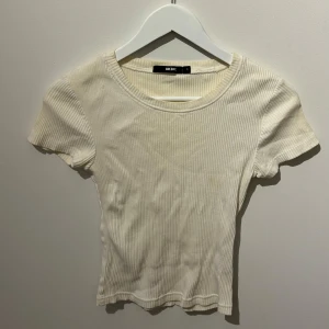 Cream vit ribbad topp från BikBok - Säljer en stilren cream vit ribbad topp från BikBok. Den har korta ärmar och en rund halsringning, perfekt för en avslappnad look. Toppen är i en mjuk och bekväm kvalitet.