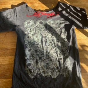 Svart Ed Hardy t-shirt med dödskalletryck - Cool svart t-shirt med ett stort tryck av flera dödskallar på framsidan. Sitter as bra och den är sne axlad eller va de heter