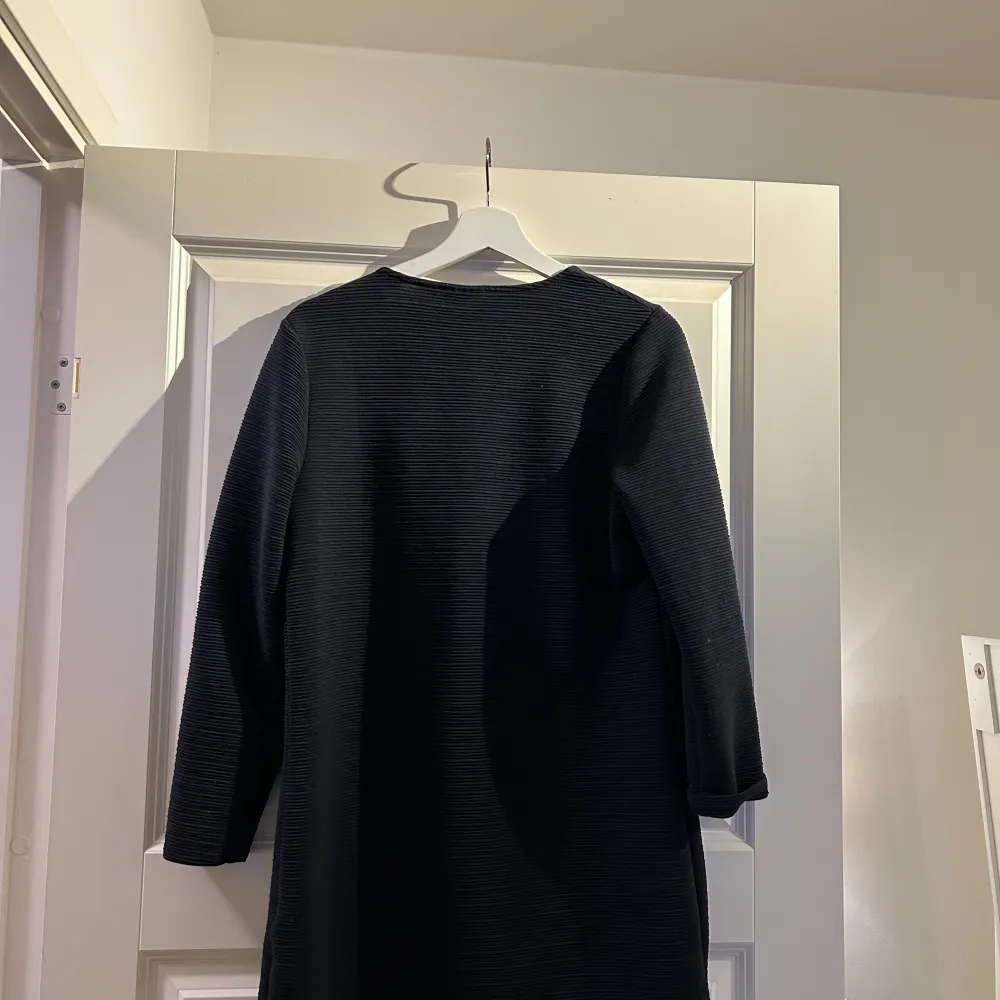 Snygg svart kappa med långärmad design och en stilren look. Perfekt för att hålla stilen i kyligare väder. Den har en enkel och elegant form som passar till många olika outfits.. Takit.