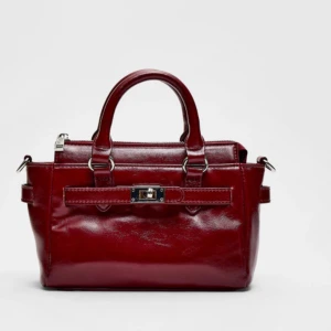 Vinröd handväska med axelrem - Röd handväska med avtagbar axelrem och spänne framtill. Väskan har en dragkedja upptill och två handtag. Använd fåtal gånger.