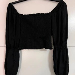 Svart offshoulder topp från Monki - Säljer en snygg svart offshoulder topp från Monki. Toppen har långa ärmar och en smockad design som ger en fin passform.