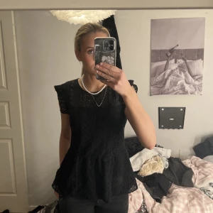 Svart spetsblus - Säljer en elegant svart spetsblus med korta ärmar och vackra spetsdetaljer. Perfekt för både vardag och festliga tillfällen. Blusen har en luftig passform och en fin knäppning i nacken.