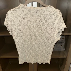 Vit spetsblus - Säljer en elegant vit spetsblus med korta ärmar. Blusen har ett vackert mönster och är perfekt för en stilren look. Passar bra till både jeans och kjol.