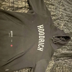 Svart hoodie från Hoodrich - Säljer en svart hoodie från Hoodrich med texten 'HOODRICH' på framsidan och 'FROM NOTHING TO SOMETHING' på baksidan. Hoodien har en stor ficka framtill och justerbar huva med snören. Perfekt för en avslappnad stil.