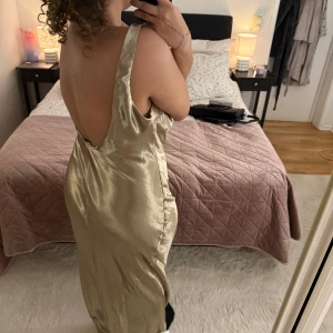 Guldig balklänning från ASOS DESIGN - Säljer en elegant guldig långklänning från ASOS DESIGN. Klänningen har en v-ringad design och är ärmlös, vilket ger en stilren och festlig look. Perfekt för speciella tillfällen där du vill glänsa. ✨