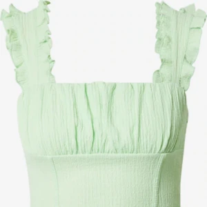 Ljusgrön topp med volangdetaljer - Säljer en söt ljusgrön topp med volangdetaljer vid axlarna. Toppen har en smickrande passform och är perfekt för varmare dagar. Materialet är mjukt och bekvämt.