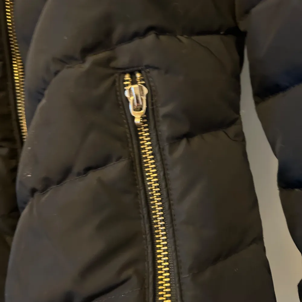 Snygg svart dunjacka från Hollies med pälsdetaljer på huvan.(äkta päls) Jackan har flera dragkedjefickor och en quiltad design. Perfekt för kyliga dagar med stil. 🖤. Takit.