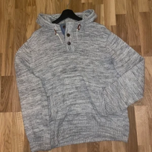 Grå stickad hoodie med knappar - Säljer en mysig grå stickad hoodie med knappar framtill och justerbar huva med snören. Perfekt för kyliga dagar. Tröjan har en avslappnad passform och ribbade muddar vid ärmslut och nederkant. Inga defekter. Storleken är M men passar M-L. 