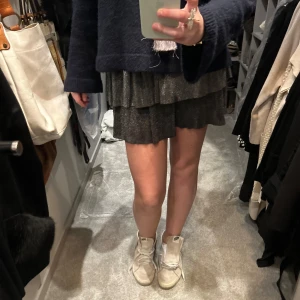 Glittrig kortkjol i lager - Snygg glittrig kortkjol i flera lager. Perfekt för att ge en festlig touch till din outfit. Kjolen har en volangdetalj som ger extra rörelse och stil.