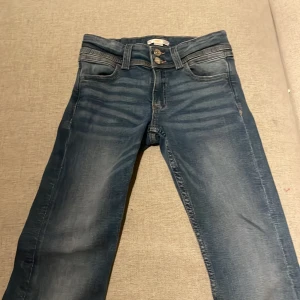 Blå jeans från Gina Tricot - Snygga blå jeans från Gina Tricot med en klassisk femficksdesign och knappar framtill. Jeansen har en lätt tvättad look och är perfekta för en avslappnad stil.