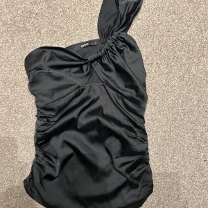 Svart oneshoulder topp från Bik Bok - Snygg svart oneshoulder topp från Bik Bok i glansigt material. Perfekt festtopp som passar till i stort sett alla underdelar!!💞💞💞