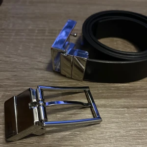 Svart bälte från Hugo - Snyggt svart bälte från Hugo med en stilren silverfärgad spänne. Bältet är gjort av skinn och har en modern design som passar perfekt till olika outfits. Spännet har en diskret Hugo-logga ingraverad. 110 cm långt. Sicka om ni har frågor om något och diskutera pris.