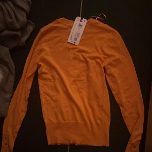 Orange tröja från Holly & White - Snygg orange tröja från Holly & white med långa ärmar och dekorativa knappar vid ärmsluten. Perfekt för att liva upp garderoben med en färgklick. Aldrig används men pris lappen kvar!! Ställ gärna frågor💕