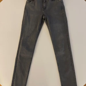 Grå jeans från Scotch & Soda - Snygga grå jeans från Scotch & Soda med klassisk design. De har en dragkedja och knapp framtill samt fickor både fram och bak. Perfekta för en stilren look. Storlek 27/32