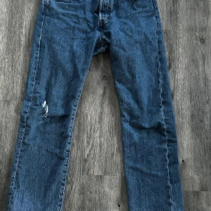 Blå jeans från Levi's - Säljer ett par klassiska blå Levi's 501 jeans. De har en rak passform och är tillverkade i slitstarkt denim. Det finns en liten reva på ena benet som ger en cool, avslappnad look.